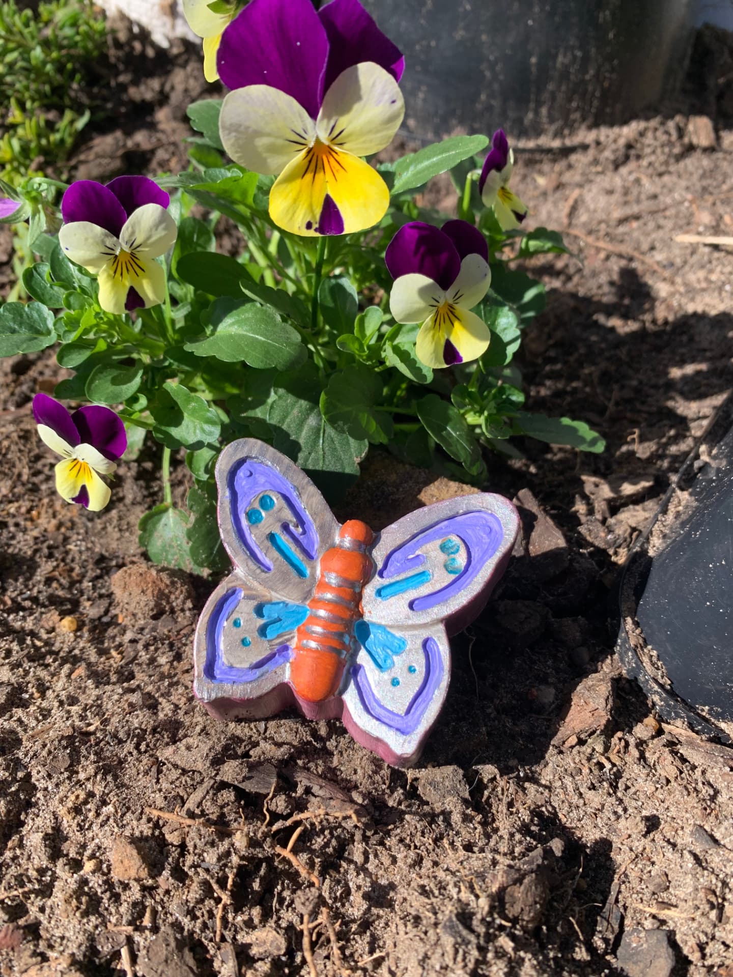 A colourful painted plaster butterfly displayed among garden flowers